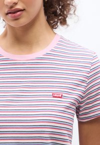 Νεαρή γυναίκα που φοράει εφαρμοστή πολύχρωμη ριγέ μπλούζα Levi's με ροζ γιακά, η οποία φαίνεται από τους ώμους έως τη μέση.