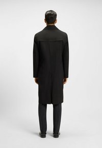 Czarny długi płaszcz z wyraźnym kołnierzem, prostym krojem i lekkim materiałem. Wyposażony w środkowy wentyl z tyłu oraz długie rękawy.