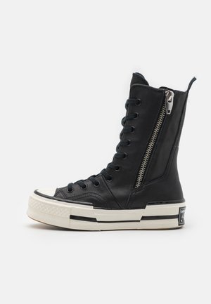 Høytopp svart lær sneakers med glidelås, rund tå, kontrasterende hvit såle og svarte snøringer, med teksturert design og logo.