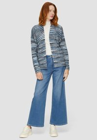 Blau gestreifter Cardigan aus weichem Stoff mit offenem Vorderdesign. Kombiniert mit weit geschnittenen Denim-Jeans und weißen Sneakers.