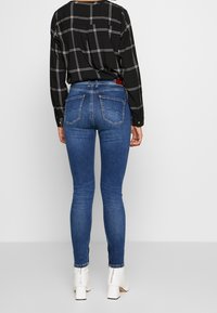 Svart rutigt långärmad skjorta i kombination med blå skinny jeans. Jeansen har en figurnära passform och bakfickor som kompletterar vita klackiga ankelboots.