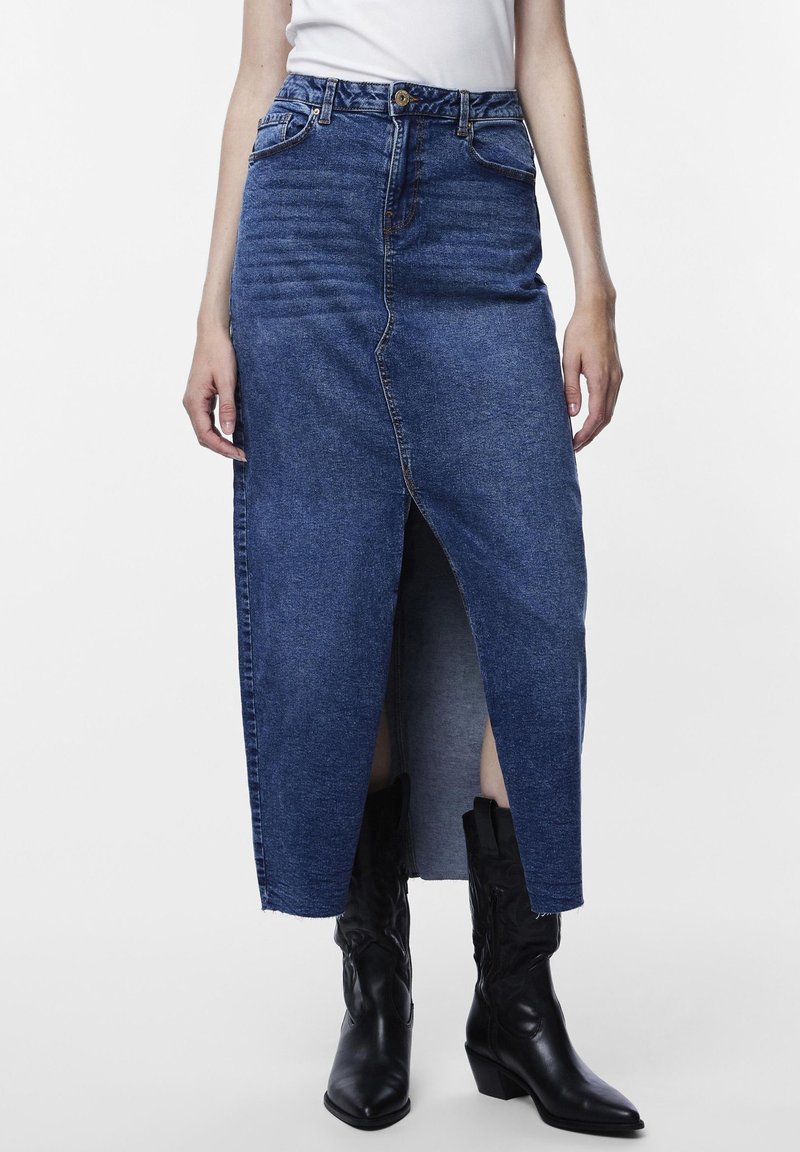 Sötétkék farmer maxiszoknya, elöl hasítékkal, fitted derékpanellel és zsebekkel, fekete cowboy csizmákkal párosítva.