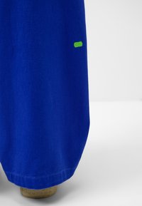 Kungligt blått tyg med en enkel design. Inkluderar en liten grön rektangulär accent på sidan. Mjuk textur, mellanlång klipp.