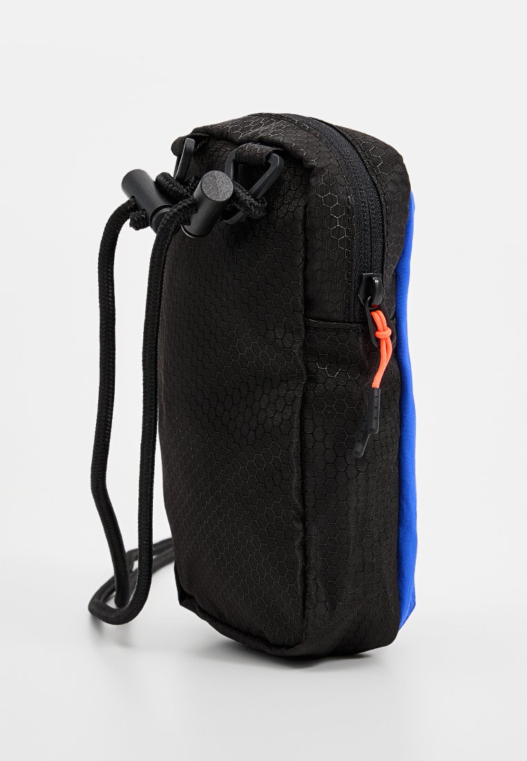 Kleine Tasche aus schwarzem Stoff mit hexagonalem Muster, blauen Seitenpanel, runder Form und seitlichem Reißverschluss mit orangefarbenem Akzent.