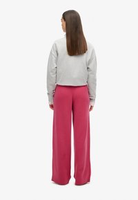 Szara krótka bluza z opuszczonymi ramionami, zestawiona z szerokimi różowymi spodniami dresowymi. Gładka tkanina, luźny krój i minimalistyczne detale.
