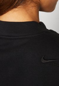 Svart sweatshirt med ribbad halsringning och en liten, prägling Nike-logotyp på  övre delen av ryggen, tillverkad av ett slätt och mjukt material.