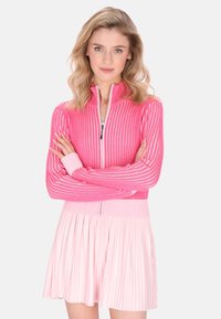 Rosa gerippte Zip-Up-Jacke mit langen Ärmeln, die abwechselnde Streifen aufweist. Kombiniert mit einem hellrosa plissierten Rock. Glatte Textur.