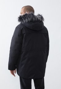 Chaqueta acolchada negra con capucha de pelo sintético. Presenta un exterior liso, capucha ajustable y puños elásticos. Diseño clásico adecuado para el invierno.