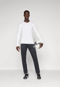 Valge, pikakäigeline, V-kujuline spordipaita, mida on paaritatud tumesiniste kitsaste pükstega. Mustad spordijalatsid ja must-valge jalgpall on kaasas.