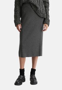 Jupe grise mi-longue en tissu tricoté doux, assortie �à un pull en tricot épais et des mocassins noirs à plateforme avec de grosses chaussettes.
