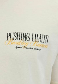 Tekst op wit textiel: "Pushing Limits Breaking Barriers Speed, Precision, Victory" in zwarte en oranje lettertypen.