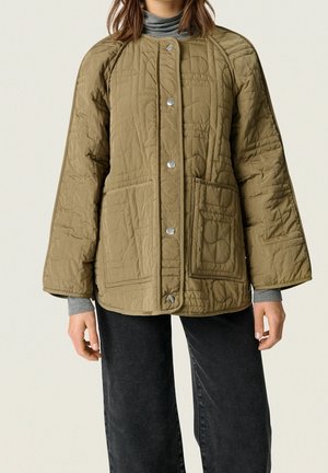 Oliwkowo-zielona pikowana kurtka na zatrzaski, z dwoma przednimi kieszeniami, noszona na szarym golfie i w połączeniu z czarnymi spodniami.