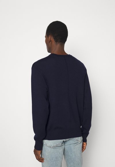 Pull en maille bleu marine avec des manches longues, un col rond et des poignets côtelés. Présente un détail de couture à l'arrière et un ourlet droit.