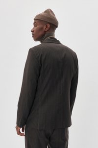 Donker gestreepte blazer met een getailleerde pasvorm, gemaakt van soepel fabric, met een enkele rugventilatie en knopen op de mouwen. Draagt een bruine gebreide muts.