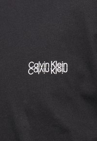 Černé bavlněné tričko s bílým logem "Calvin Klein", zobrazeným v zrcadlovém stylu, s hladkou strukturou.