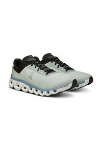 Hellgraue Sportschuhe mit schwarzen Akzenten, textiles Obermaterial, strukturiertes Design, gepolsterte Sohle und segmentierte Sohlenbereiche für Flexibilität.
