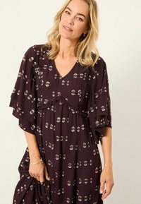 Lila Kleid mit Rüschendetails und kurzen Ärmeln, das ein gepunktetes Goldmuster aufweist. Hergestellt aus leichtem Stoff, mit einem V-Ausschnitt gestaltet.