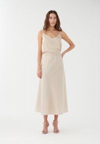 Vestido de satén beige con escote en V, tirantes de espagueti ajustables y cintura elástica. Falda fluida hasta los tobillos. Tacones plateados con tiras.