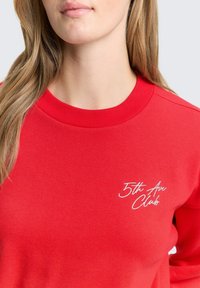 Rode sweatshirt van zachte stof, met een ronde hals, geribbelde manchetten en een geborduurd wit "5th Ave Club" logo op de borst.