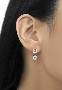 Boucles d'oreilles en or en forme de créoles, ornées d'un petit cristal rond et d'un plus grand cristal carré suspendu en dessous, le tout sur une oreille lisse.