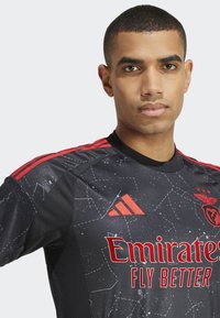 Juodas sportinis marškinėliai su raudonomis detalėmis, turintys tekstūruotą žvaigždžių raštą, „Adidas“ logotipą ir raudoną tekstą „Emirates Fly Better“.