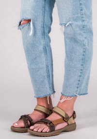 Bruna och tanfärgade sandaler med remmar och justerbara band samt texturerade sålar, i kombination med ljusblå, slitna jeans med fransar vid fållarna.