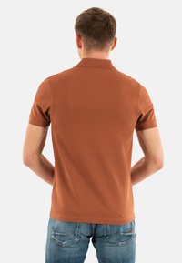 Bruine polo gemaakt van zachte stof, met een klassieke kraag en korte mouwen, gecombineerd met denim jeans.