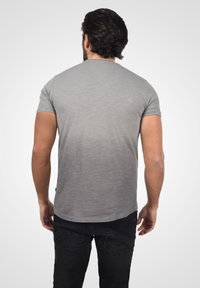 Grå t-skjorte med korte ermer og en lett buet søm, med subtil tekstur, kombinert med svarte jeans, sett fra baksiden.