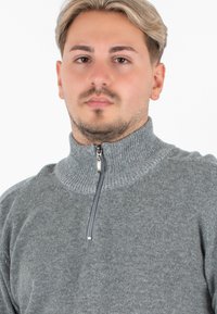 Maglione grigio con cerniera e colletto alto, realizzato in tessuto a maglia texturizzato. Caratterizzato da una cerniera a metà e dettagli a costine sul colletto.