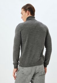 Grå tröja med hög krage, ribbade mudd och nederkant. Tajt design, tillverkad av mjukt material, visad från baksidan mot en enkel bakgrund.