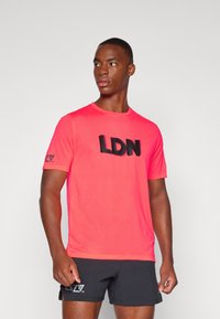 Tricou din plasă roz aprins, cu un imprimeu negru îndrăzneț "LDN" pe față și detaliu cu logo pe manșetă. Guler rotund și mâneci scurte.