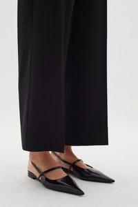 Svarta slingback-lägenheter med spetsig tå, glänsande yta och dubbla remmar över fotryggen. Stylad med svarta vida byxor.