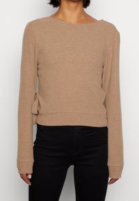 Beige ribbad stickad tröja med båt-nacke, långa ärmar och en sidenotering på sidan, kombinerat med svarta tajta jeans.