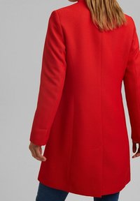 Rode, gestructureerde wollen jas met een rechte snit, lange mouwen en een hoge halslijn, zonder sluitingen of zichtbare zakken.