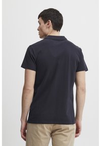 Navy blue polo shirt in cotton, featuring a collar and short sleeves. Back view shows smooth texture and minimal branding details.
