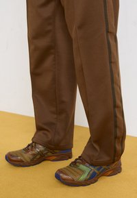 Bruna sportbyxor med sidosträck, matchade med mångfärgade löparskor med meshtopp, strukturerad design och vadderade sulor.