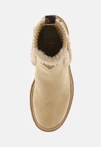 Beżowy zamszowy botek za kostkę z puszystym kołnierzem i gumową podeszwą. Widoczne wnętrze, z małą czarną etykietą z tyłu.