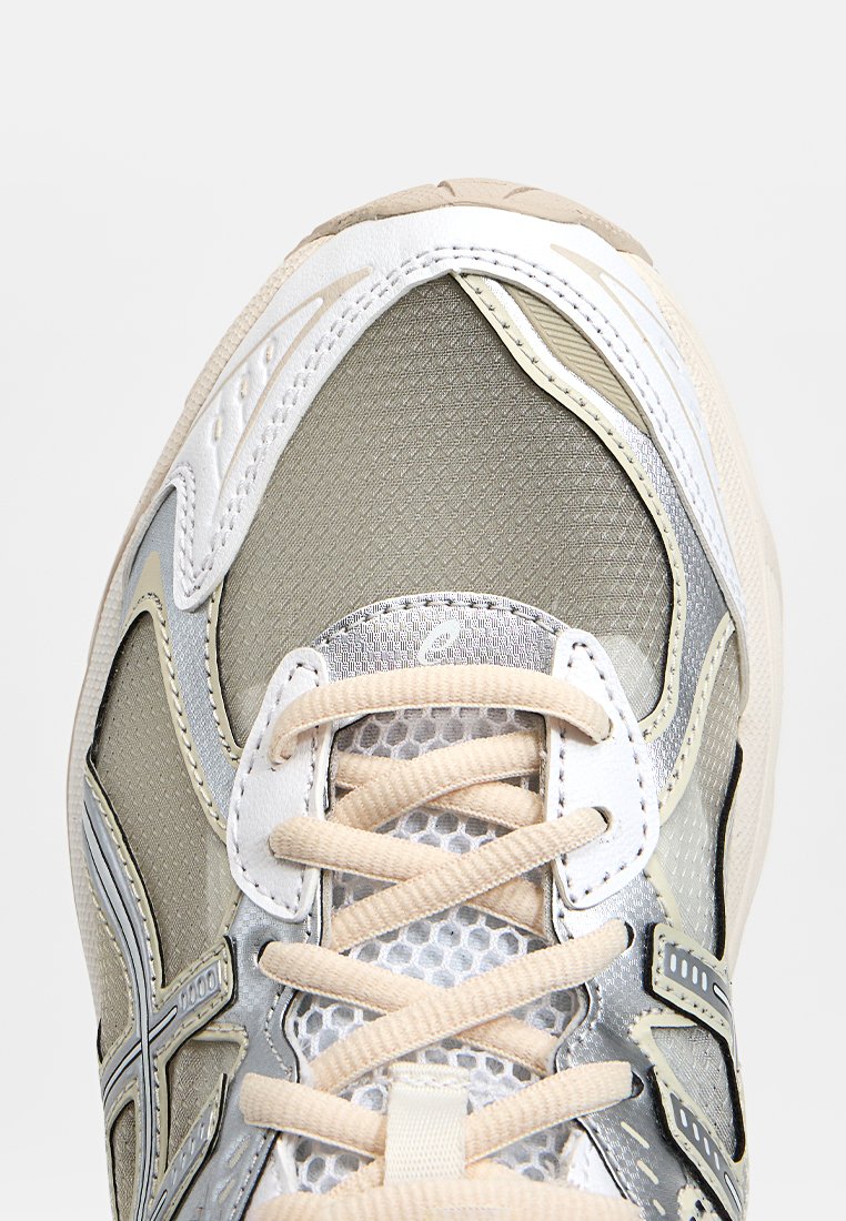 Lichte hardloopschoen met een bovenwerk van mesh in beige en grijs met zilveren accenten, ronde neus en beige veters over een gevoerde tong.