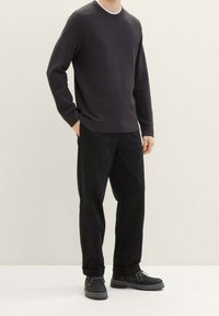 Maglione a maglia testurizzata blu marino con maniche lunghe, abbinato a pantaloni neri e scarpe nere con lacci e suole robuste.