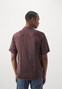 Chemise à manches courtes en tissu bordeaux foncé, avec une texture lisse et un col classique, à ourlet droit et coupe décontractée.