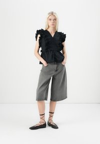 Top nero a maniche puff con dettagli a balze, abbinato a culotte grigie a gamba larga e scarpe nere flat con cinturini incrociati.