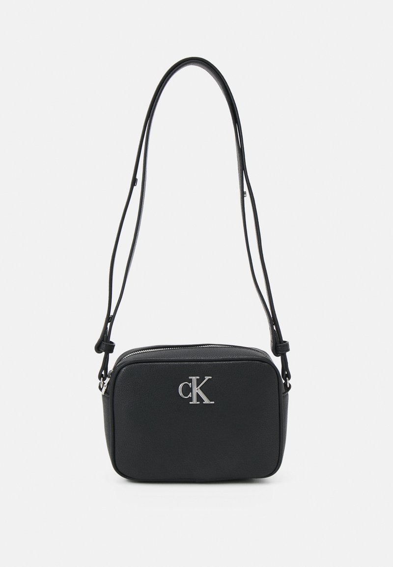 Borsa a mano nera in materiale testurizzato. Presenta un logo "cK" argentato, chiusura con zip e tracolle regolabili. Forma rettangolare compatta.