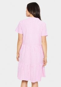 Robe rayée verticalement rose et blanche avec des manches courtes, taille froncée et jupe à volants, fabriquée en tissu léger. Vue arrière présentée.