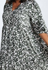 Robe fleurie avec un motif vert et blanc, coupe décontractée, manches mi-longues, corsage plissé et jupe à plusieurs niveaux.