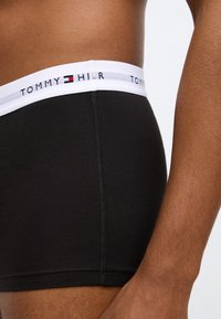 Boxer in cotone nero con cintura bianca che presenta il logo "TOMMY H". Superficie liscia e design aderente con cuciture a contrasto.