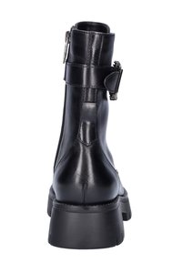 Botín negro de cuero con suela gruesa, cremallera lateral y un detalle de correa con hebilla. Textura suave y diseño ajustado.