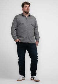 Button-up shirt in zwart-wit geometrisch patroon, lange mouwen, gecombineerd met donkere spijkerbroek en witte sneakers met zwarte accenten.