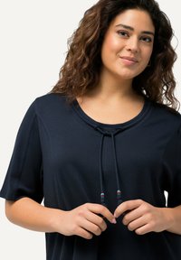 Top blu navy a maniche corte con scollatura rotonda, dotato di un cordoncino con decorazioni in perline, realizzato in tessuto morbido.