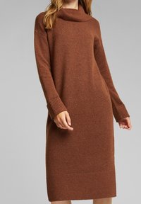 Abito marrone lavorato a maglia con scollatura a cowl, polsini e orlo a coste. Maniche lunghe, forma aderente e texture morbida.