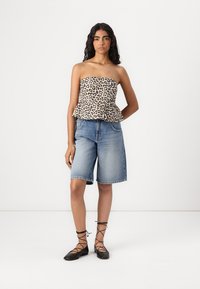 Top brez naramnic z vzorcem leoparda, peplum oblikovanja, v kombinaciji z svetlo modrimi jeans kratkimi hlačami. Model nosi črne čipkaste balerinke.